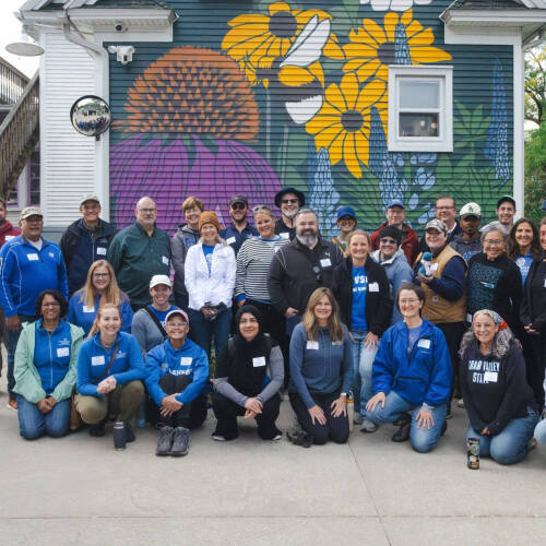 large group of people standing and sitting outside a building that has a mural of flowers painted on it